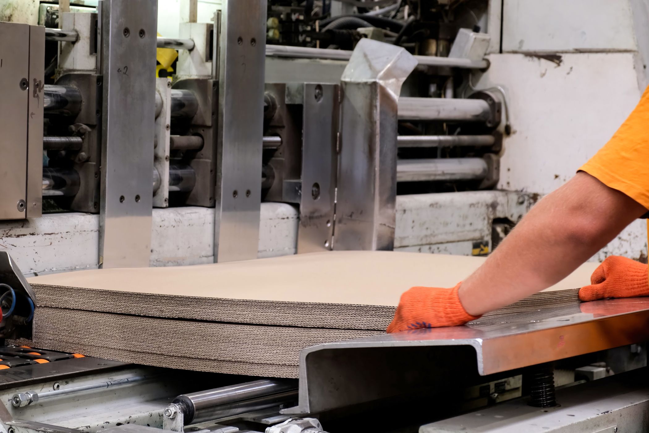 Gloved hands feeding a stack of corrugated board into a production machine